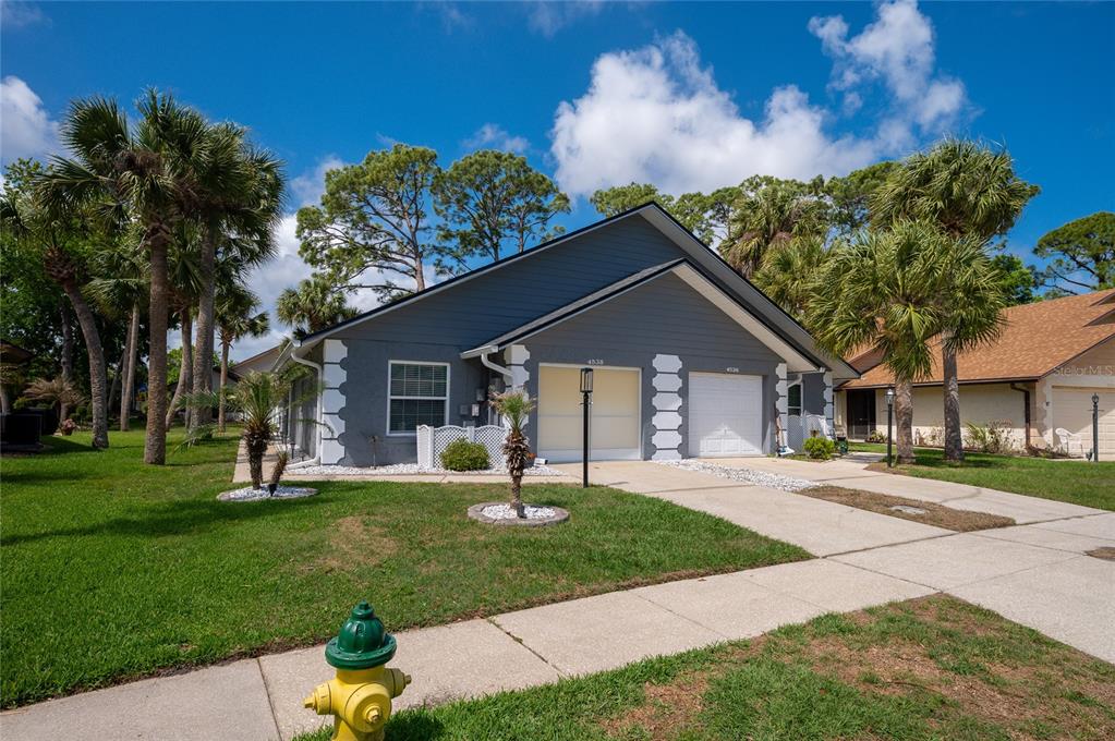 A gray duplex with white trim and two garage doors sits behind a grassy lawn — 4538 ROCKLEDGE LANE, PORT ORANGE, FL