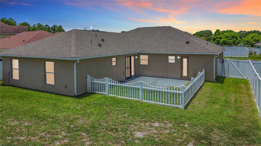The exterior rear view of a house features a concrete patio and a white fence — 3013 MANDOLIN DRIVE, KISSIMMEE, FL