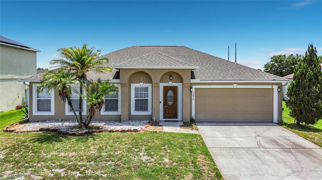 A single-story house with a tan stucco exterior, a two-car garage, and a palm tree — 3013 MANDOLIN DRIVE, KISSIMMEE, FL