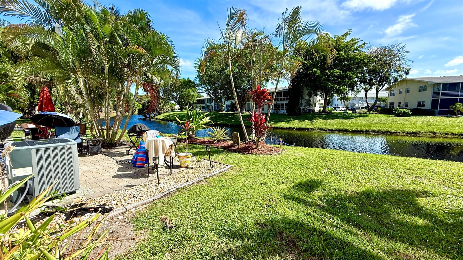 A patio with a grill and seating overlooks a canal surrounded by grass and trees — 79 Lyndhurst D, Deerfield Beach FL 33442, DEERFIELD BEACH, FL