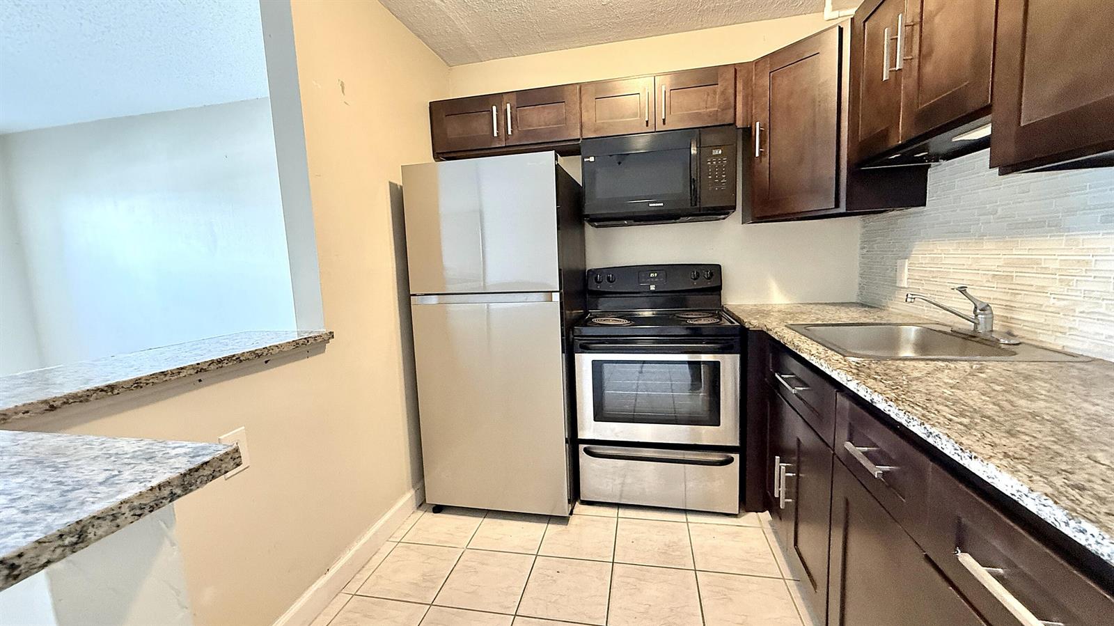 A kitchen features dark wood cabinets, stainless steel appliances, and granite countertops — 79 Lyndhurst D, Deerfield Beach FL 33442, DEERFIELD BEACH, FL