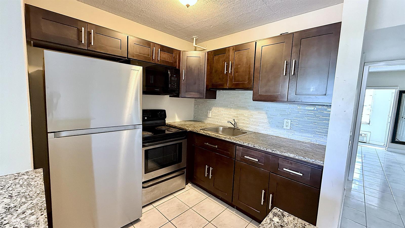 A kitchen features dark wood cabinets, stainless steel appliances, granite countertops, and a tiled floor — 79 Lyndhurst D, Deerfield Beach FL 33442, DEERFIELD BEACH, FL