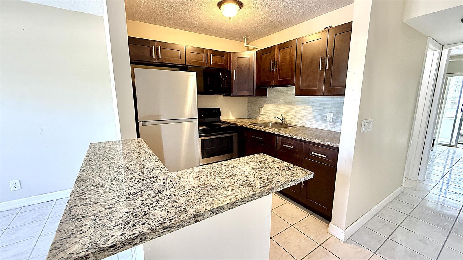 A kitchen features dark wood cabinets, granite countertops, stainless steel appliances, and tile flooring — 79 Lyndhurst D, Deerfield Beach FL 33442, DEERFIELD BEACH, FL
