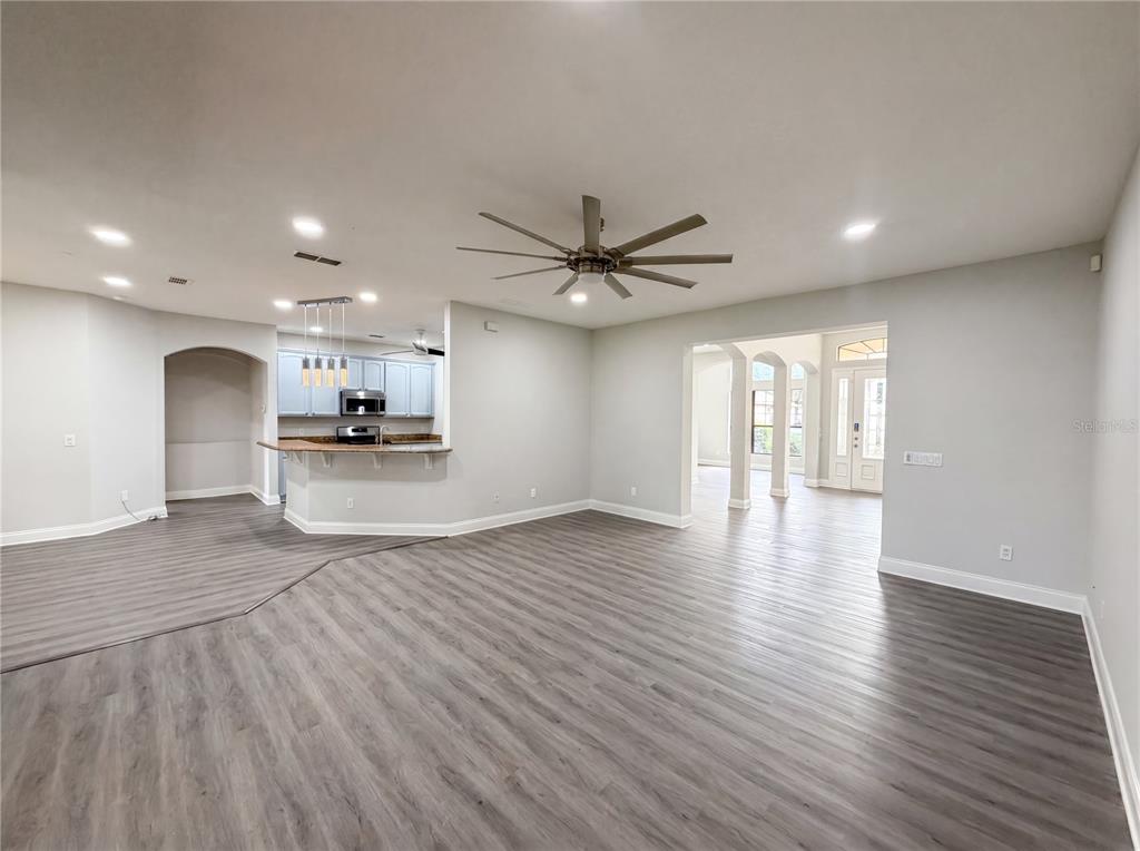 A spacious living area with gray wood-look flooring, a ceiling fan, and an open kitchen — 216 BLUE CRYSTAL DRIVE, DELAND, FL