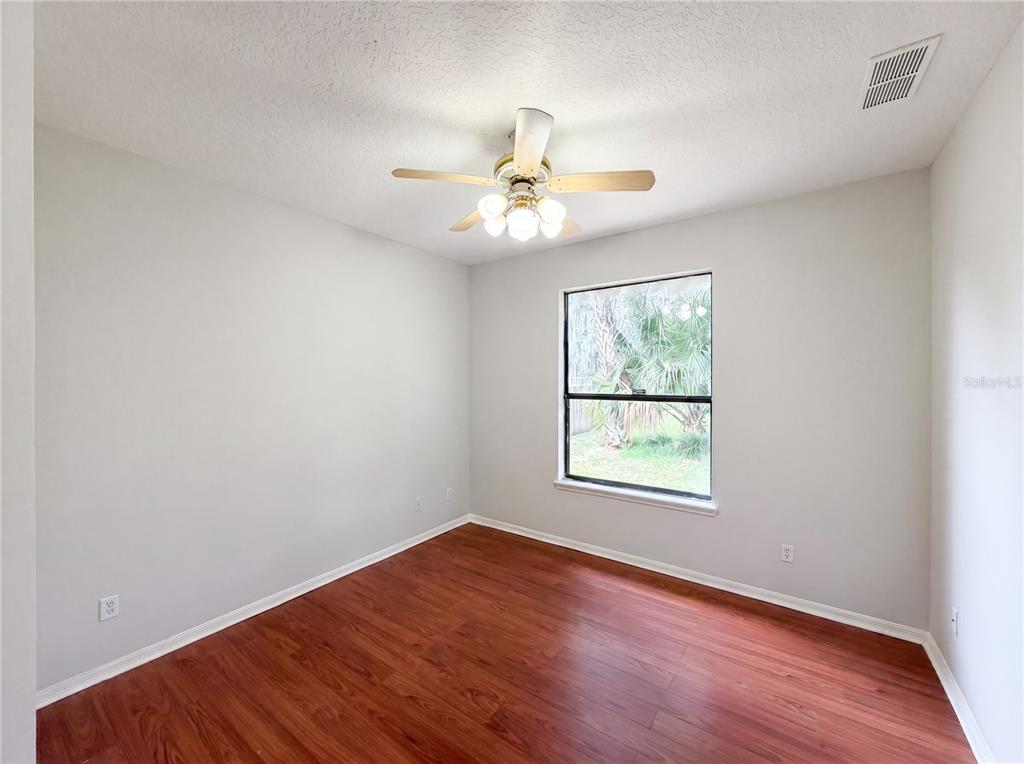 A bedroom with light gray walls, wood-look flooring, a ceiling fan, and a single window — 216 BLUE CRYSTAL DRIVE, DELAND, FL