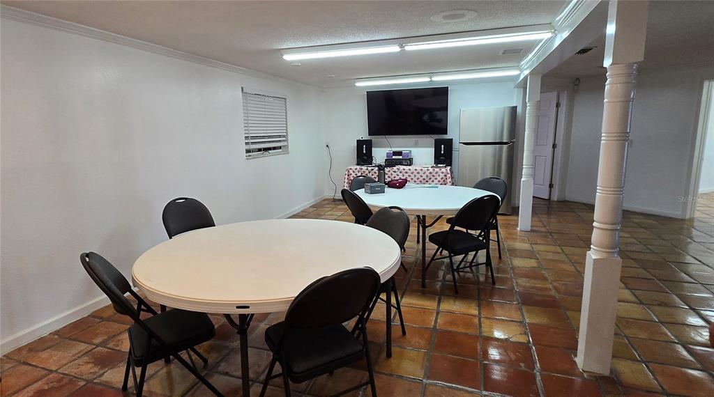 A room with two round tables, black folding chairs, tile flooring, and a stainless refrigerator — 8814 ROCKY CREEK DRIVE, TAMPA, FL
