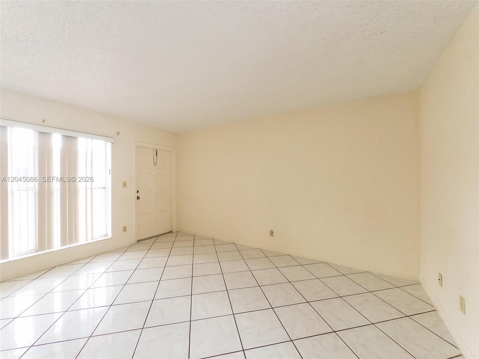 An empty room features white tiled floors, beige walls, and a white entry door — 5870 NW 16th Pl # 4, Sunrise FL 33313, SUNRISE, FL
