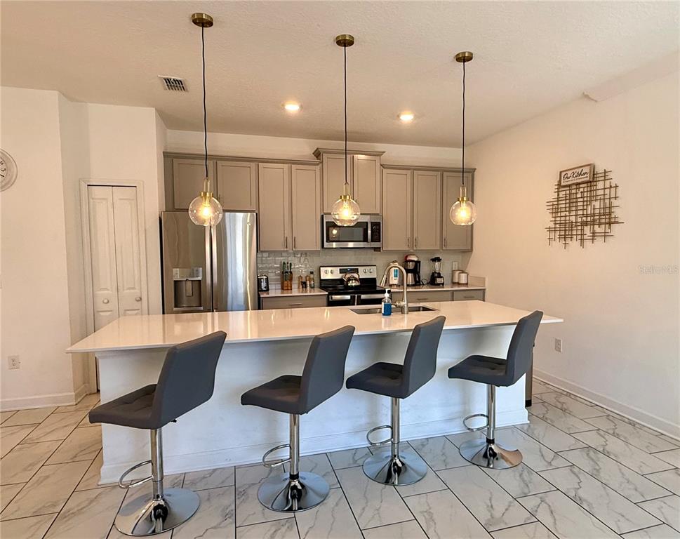 A kitchen features a white island with four gray bar stools and light-colored cabinetry — 4190 PARAGRAPH DRIVE, KISSIMMEE, FL