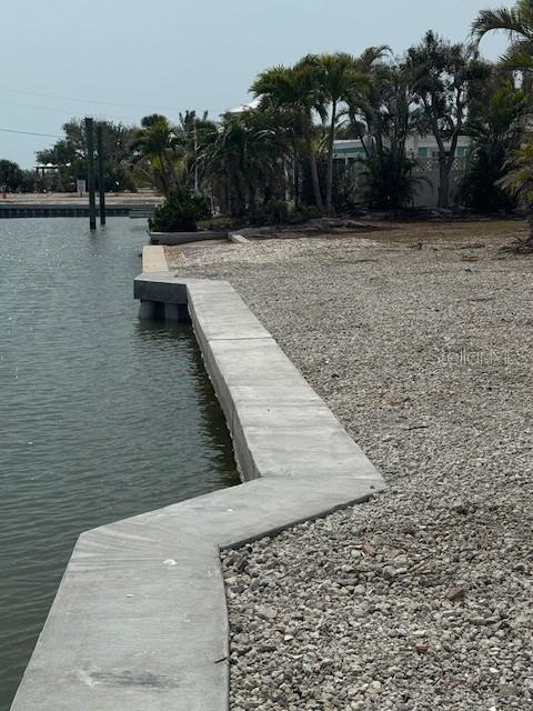 A concrete seawall borders a gravel shoreline next to a canal with palm trees — 1285 HOLIDAY DRIVE, ENGLEWOOD, FL
