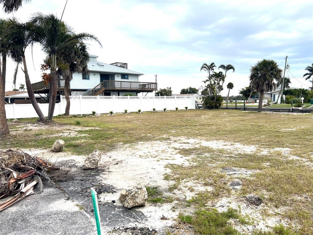 A vacant, grassy lot features scattered rocks and palm trees near a white fence — 1285 HOLIDAY DRIVE, ENGLEWOOD, FL