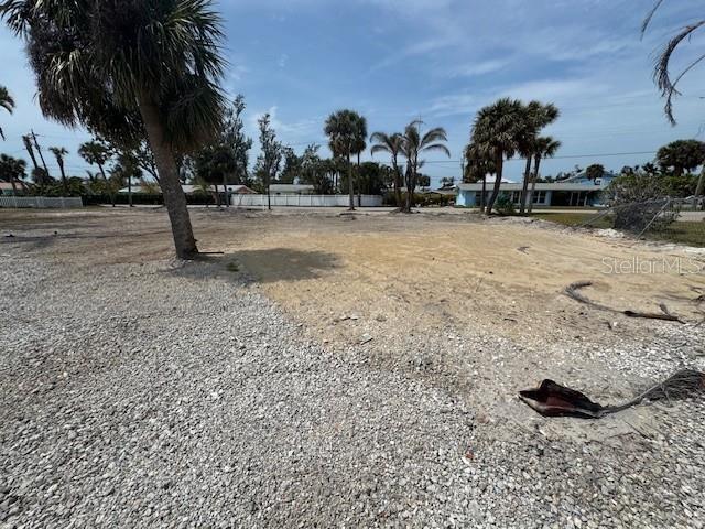 A vacant, sandy lot features scattered gravel and several palm trees under a blue sky — 1285 HOLIDAY DRIVE, ENGLEWOOD, FL