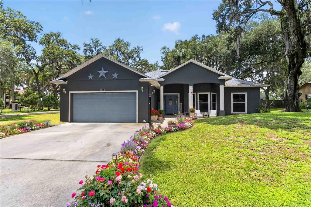 A dark gray single-story house with a two-car garage, front porch, and landscaped flower beds — 1260 PECAN STREET, KISSIMMEE, FL