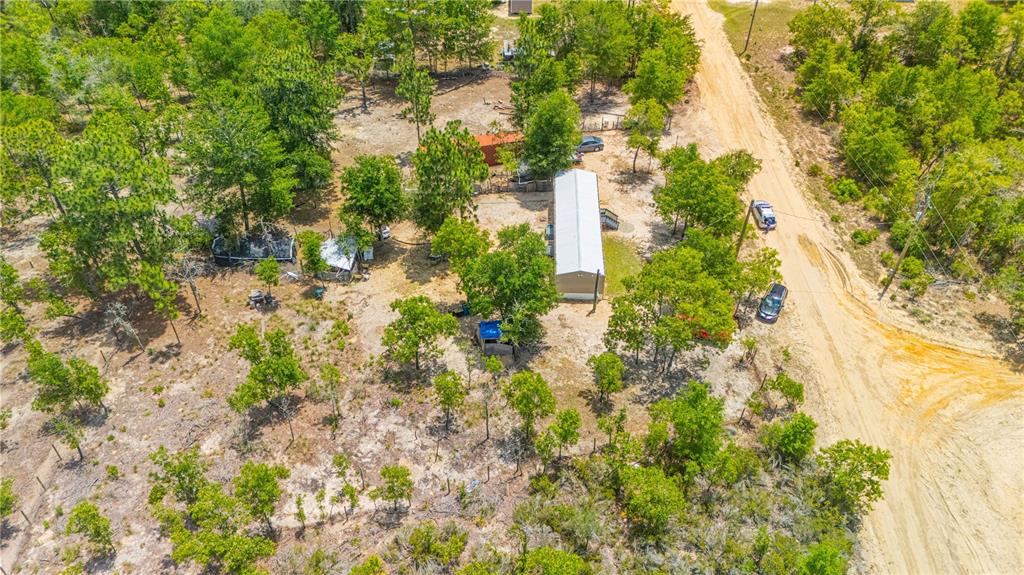 An aerial view shows a long rectangular house on a wooded lot with a dirt road — 116 LONDON AVENUE, INTERLACHEN, FL