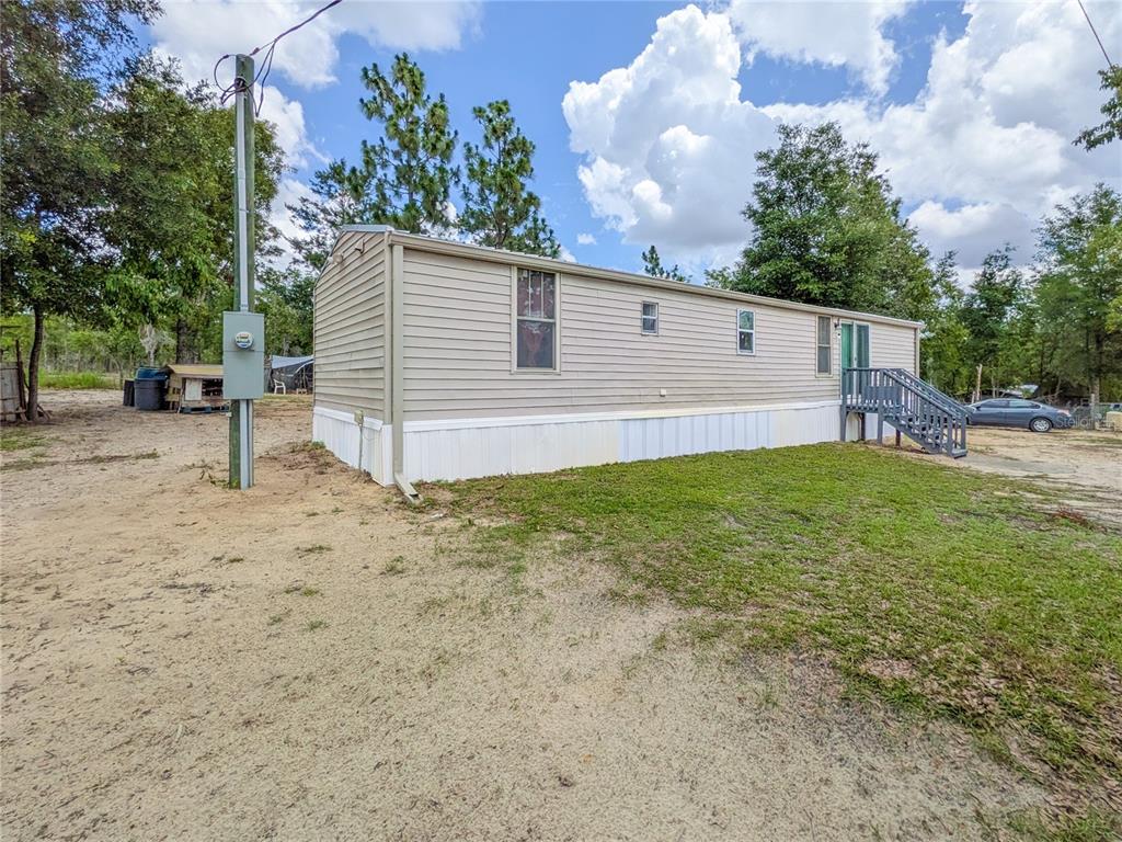 A beige mobile home with a small wooden deck sits on a sandy, grassy lot — 116 LONDON AVENUE, INTERLACHEN, FL