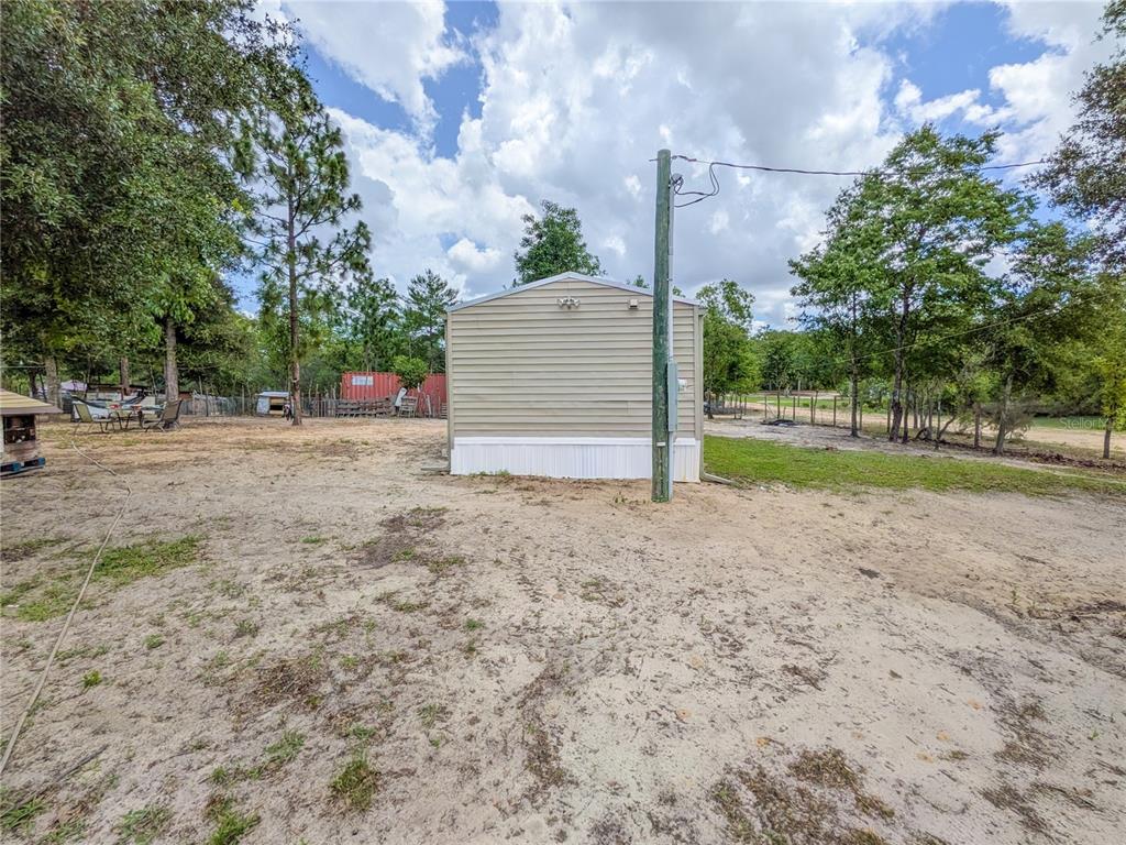 The exterior of a beige mobile home sits on a sandy lot with trees nearby — 116 LONDON AVENUE, INTERLACHEN, FL