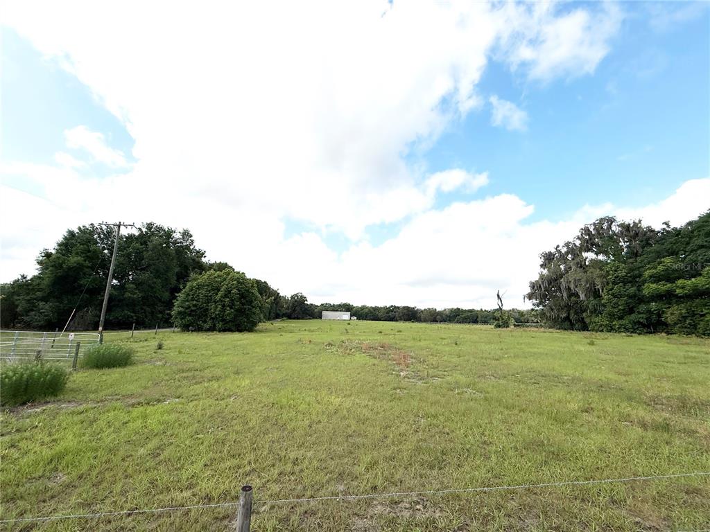 A wide, grassy field is bordered by trees under a partly cloudy sky — SE SUNSET HARBOR ROAD, WEIRSDALE, FL