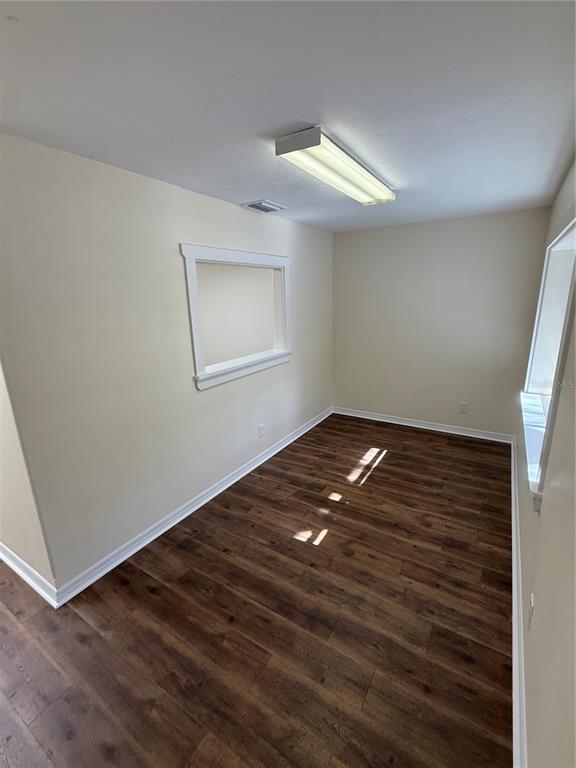 An empty room features light-colored walls, dark wood-look flooring, and a rectangular ceiling light — 108 NW 10TH AVENUE, WILLISTON, FL