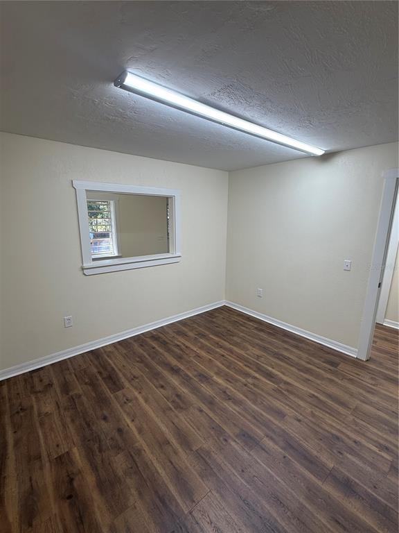 An empty room with wood-look flooring, cream walls, a rectangular wall cutout, and a ceiling light — 108 NW 10TH AVENUE, WILLISTON, FL