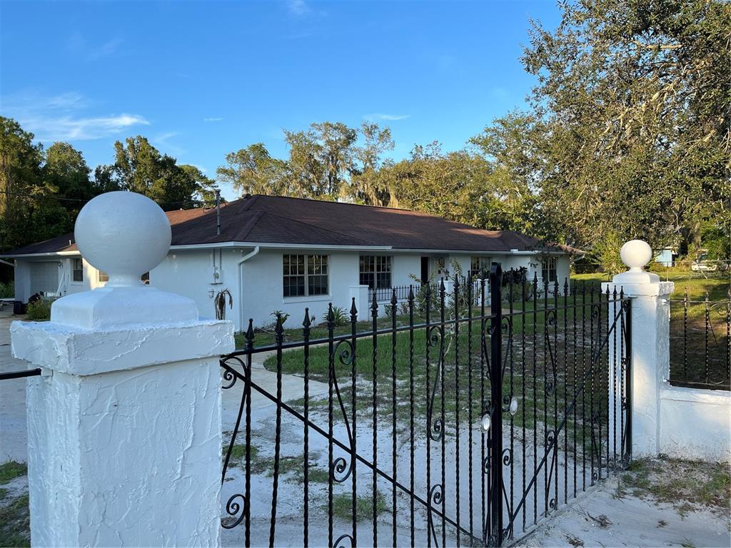 A white, single-story house is viewed from behind a black metal gate and stone pillars — 230 BAY MEADOW ROAD, LONGWOOD, FL