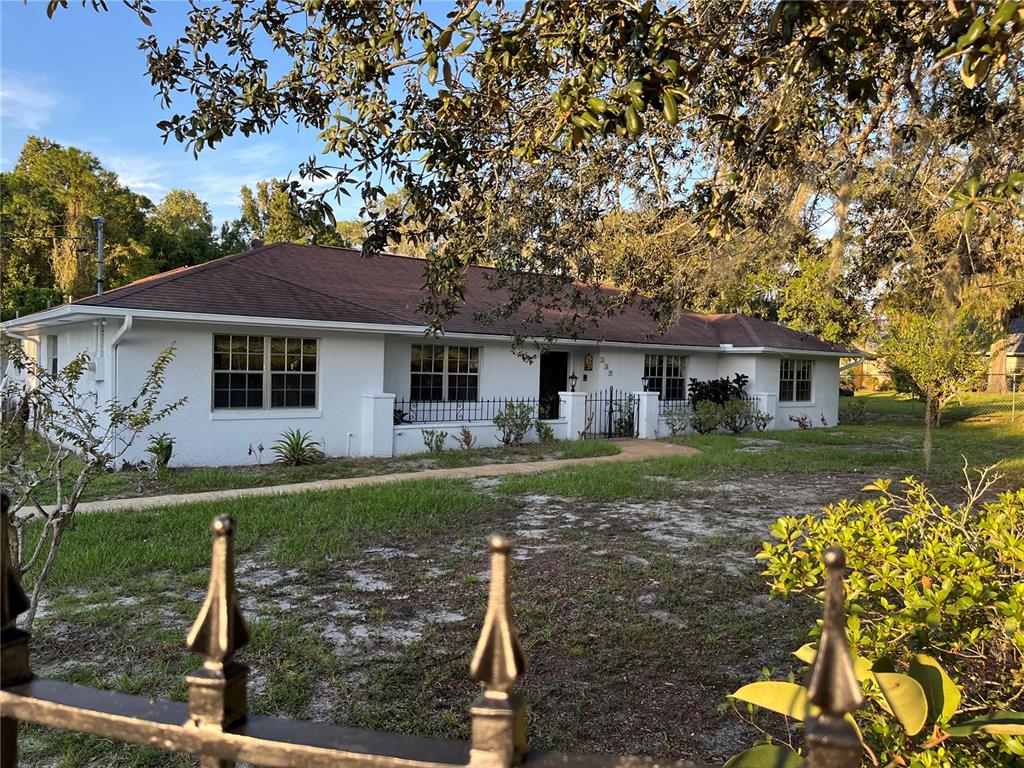 A single-story white house with a brown roof sits behind a black metal fence — 230 BAY MEADOW ROAD, LONGWOOD, FL