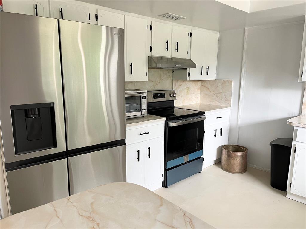 A kitchen features white cabinets, stainless steel appliances, and light-colored countertops with a marble pattern — 230 BAY MEADOW ROAD, LONGWOOD, FL