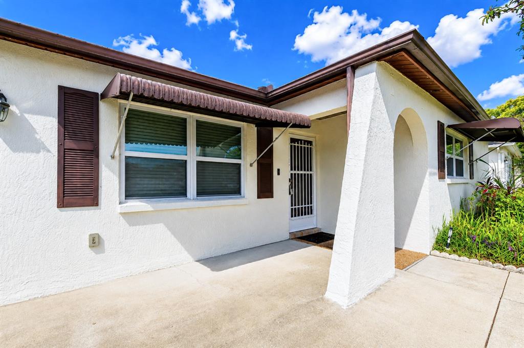A white stucco house exterior features a covered porch, brown awnings, and a security screen door — 8811 MARTINIQUE LANE, PORT RICHEY, FL
