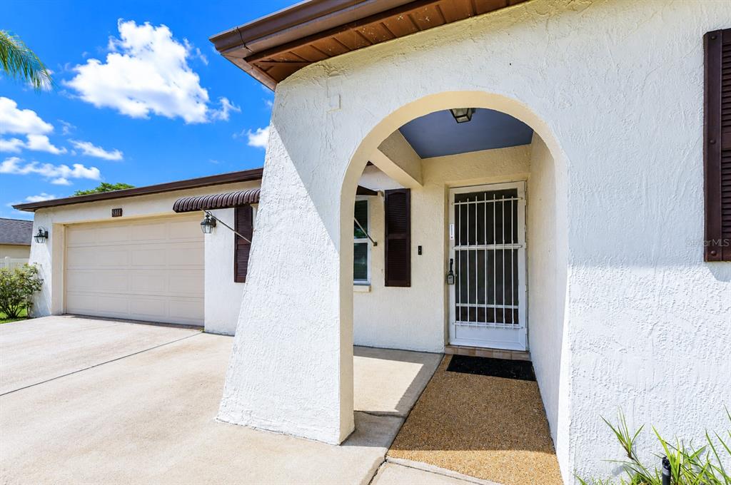 A white stucco house exterior features an arched entryway, a garage, and brown shutters — 8811 MARTINIQUE LANE, PORT RICHEY, FL