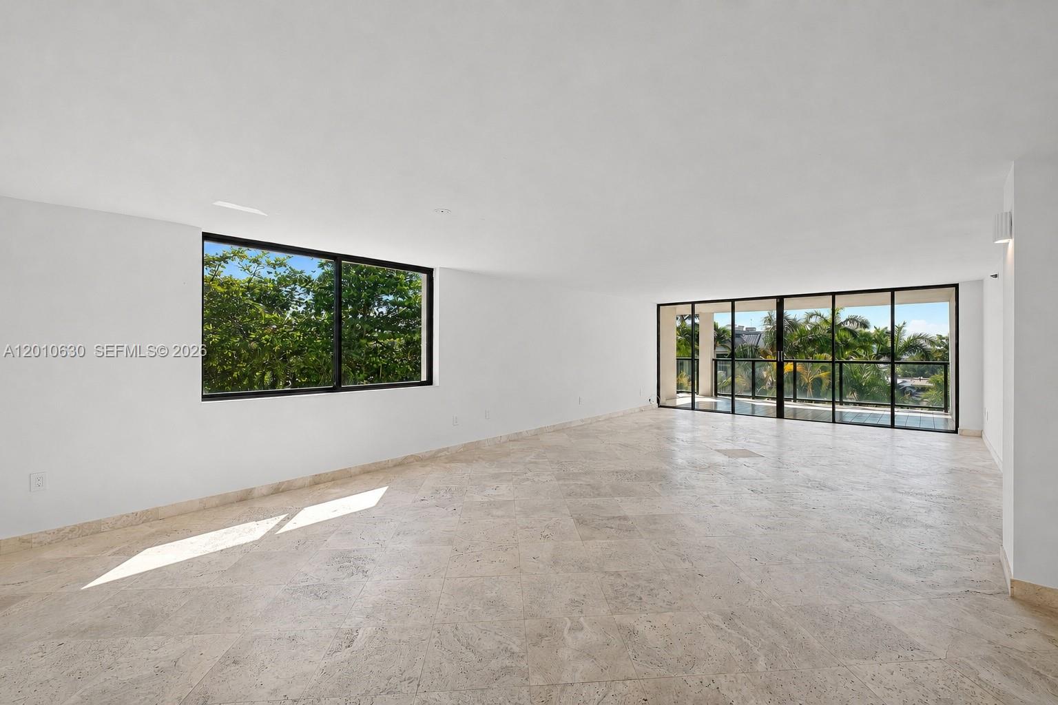An empty room features light-colored tile flooring, white walls, and large windows overlooking trees — 2575 S Bayshore Dr # 4A, Miami FL 33133, MIAMI, FL