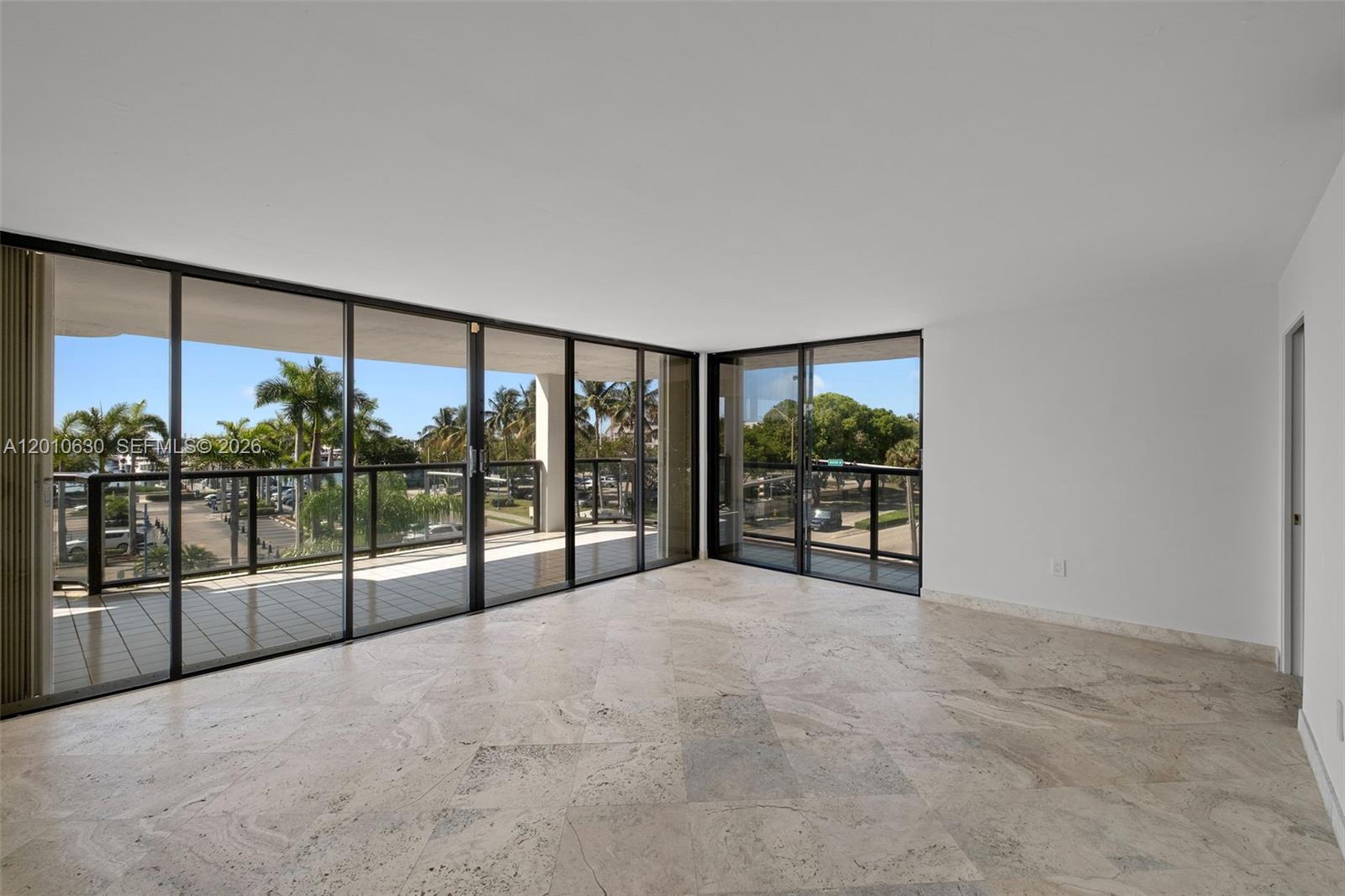 An empty room with marble floors and floor-to-ceiling windows overlooking a balcony and trees — 2575 S Bayshore Dr # 4A, Miami FL 33133, MIAMI, FL