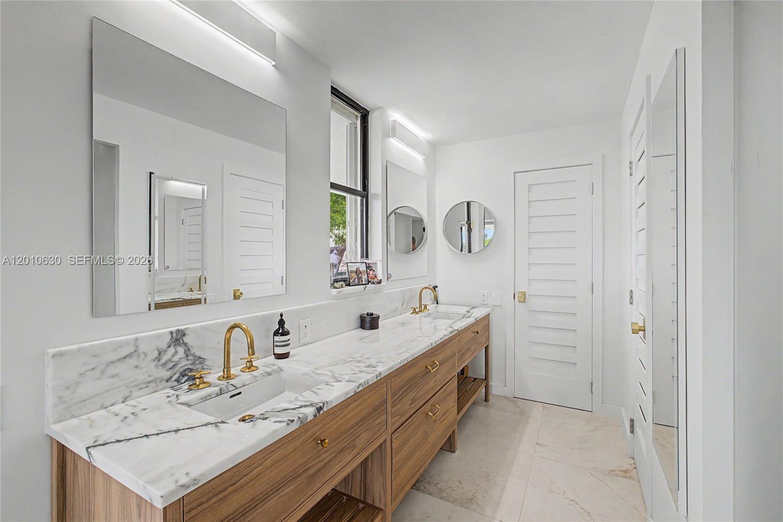 A modern bathroom features a double vanity with marble countertops, wood cabinetry, and gold fixtures — 2575 S Bayshore Dr # 4A, Miami FL 33133, MIAMI, FL