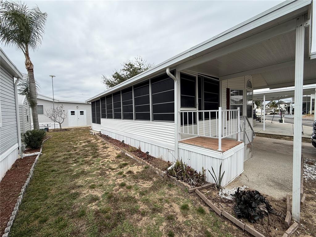 The exterior of a mobile home features a screened-in porch, a carport, and landscaping — 231 ST GEORGE DRIVE, DAVENPORT, FL