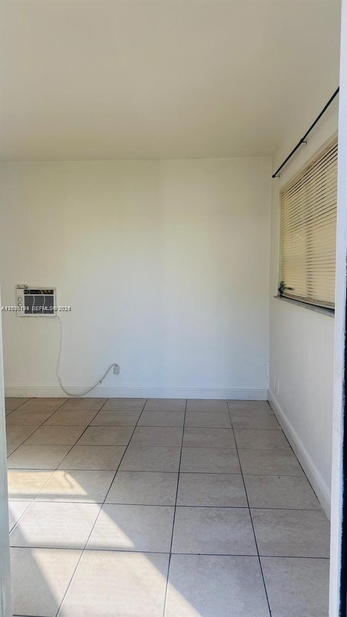 An empty room features white walls, light-colored tile flooring, a window with blinds, and a wall-mounted air conditioner — 1321 NW 50th Ave # A, Lauderhill FL 33313, LAUDERHILL, FL