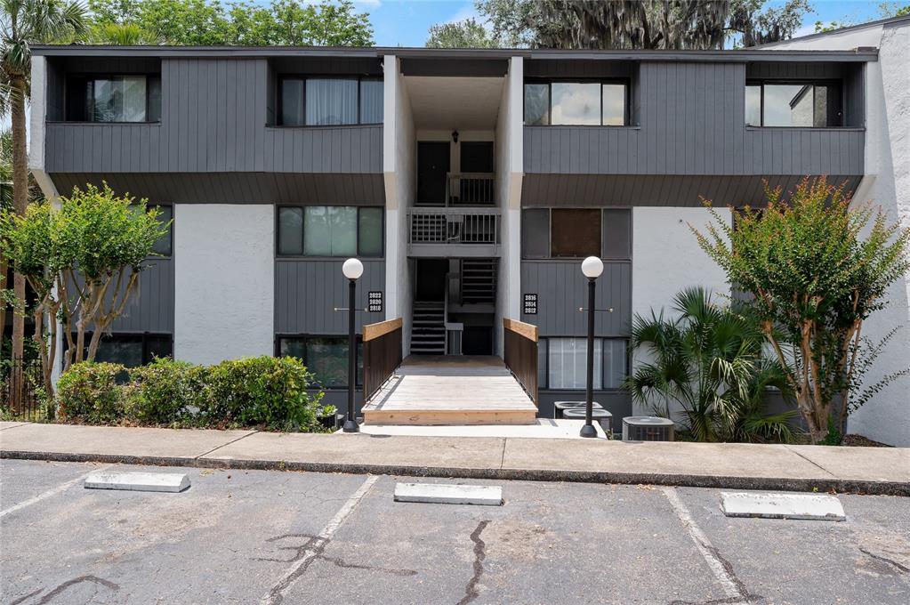 A two-story apartment building features a central wooden walkway leading to an open stairwell — 2818 SW 14TH DRIVE UNIT 107, GAINESVILLE, FL