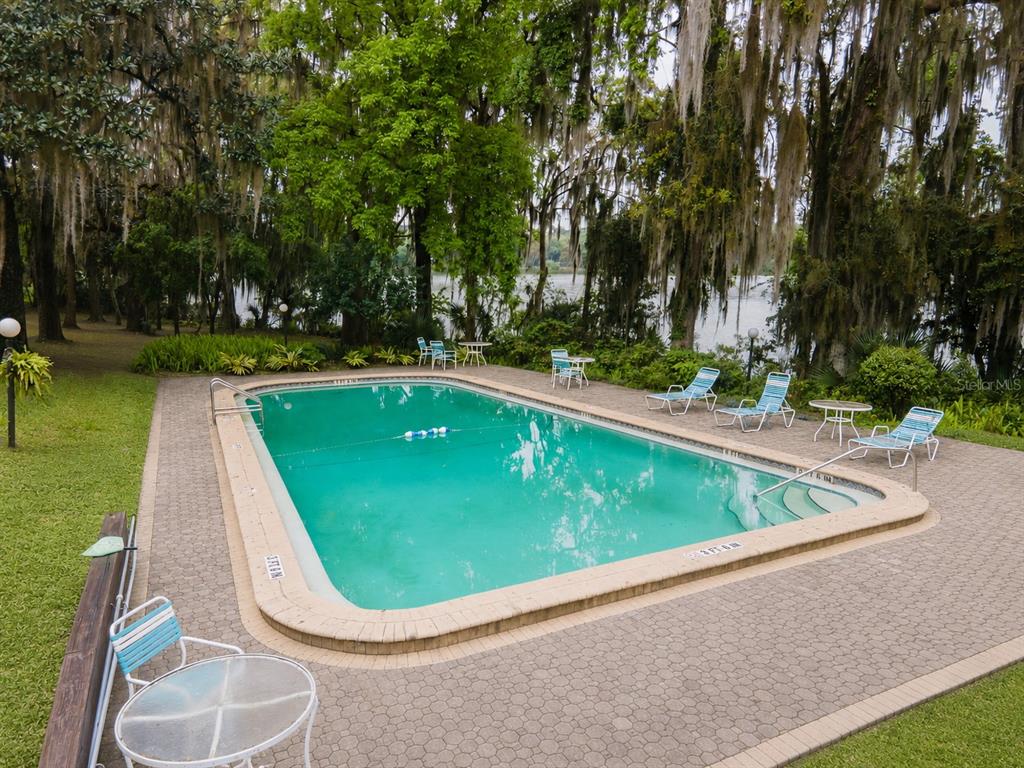 A rectangular swimming pool sits on a paved patio surrounded by trees and a lake — 2818 SW 14TH DRIVE UNIT 107, GAINESVILLE, FL