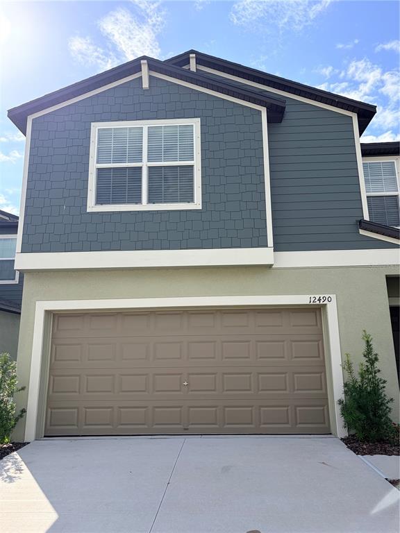 A two-story house exterior features a tan garage, blue siding, and a shingled upper facade — 12490 SWEET ANGEL AURA WAY, PARRISH, FL