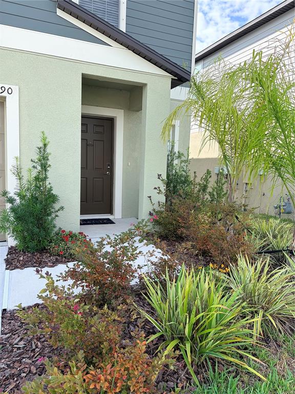 A light green house exterior features a dark brown front door and landscaped garden beds — 12490 SWEET ANGEL AURA WAY, PARRISH, FL