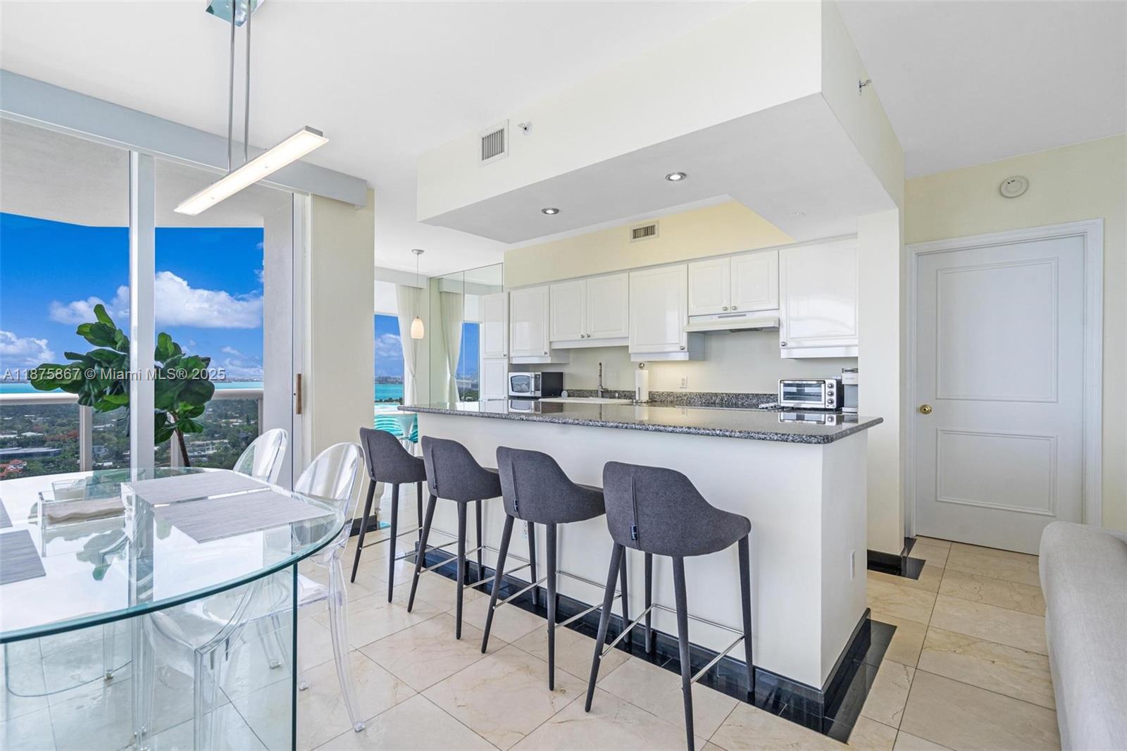 A kitchen with white cabinets and a granite breakfast bar overlooks a dining area — 4779 Collins Ave # 2305, Miami Beach FL 33140, MIAMI BEACH, FL