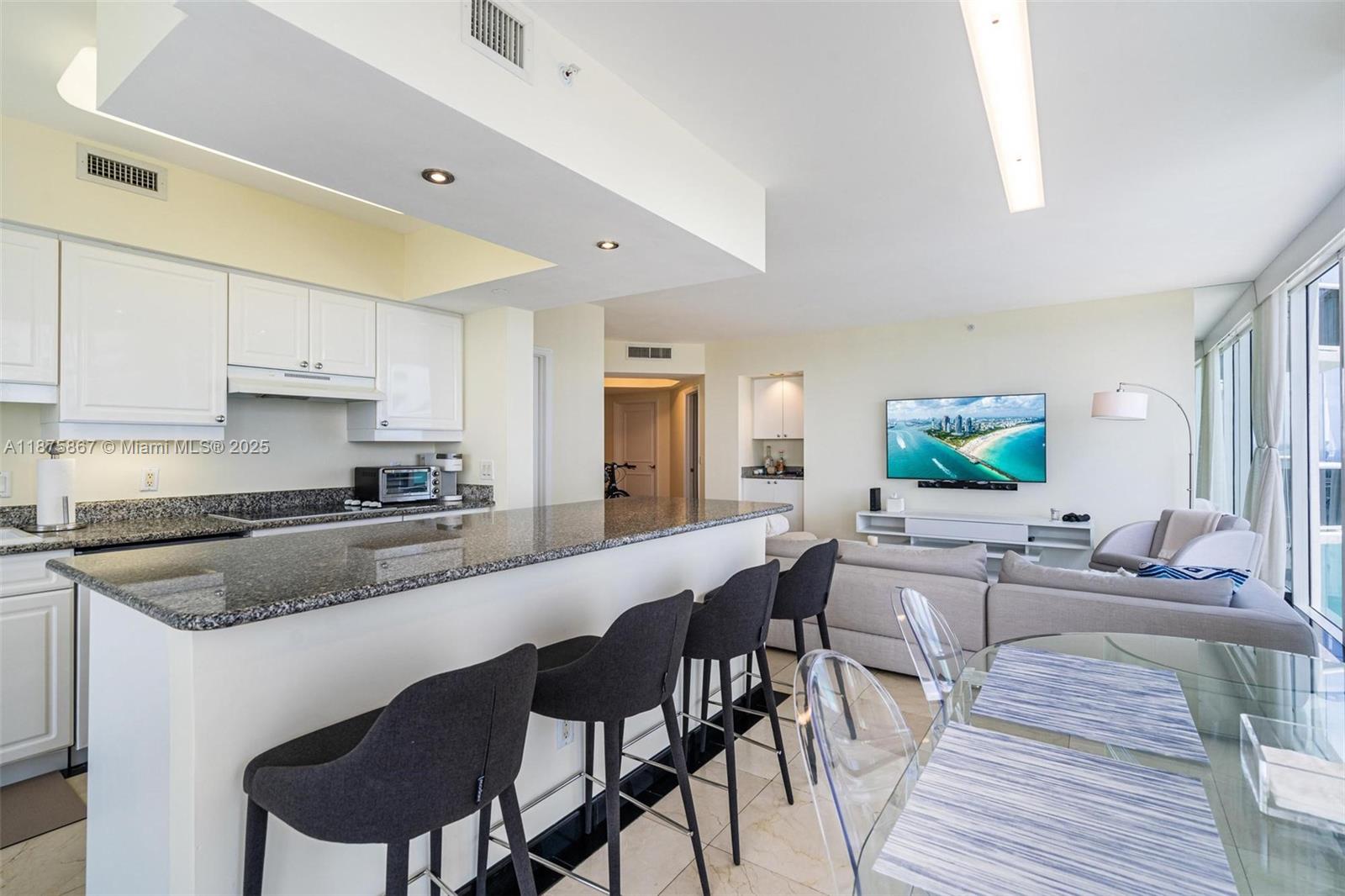 A kitchen with granite countertops and bar stools overlooks a living area with a television — 4779 Collins Ave # 2305, Miami Beach FL 33140, MIAMI BEACH, FL