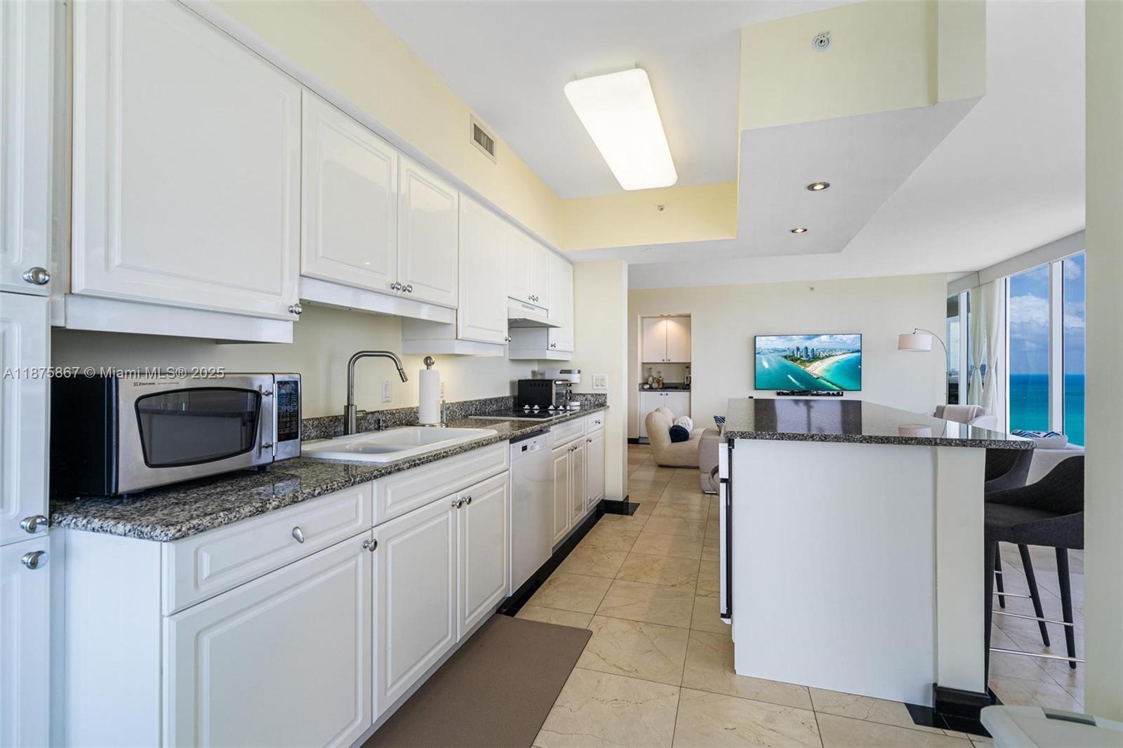 A white kitchen features granite countertops, stainless steel appliances, and an island overlooking the ocean — 4779 Collins Ave # 2305, Miami Beach FL 33140, MIAMI BEACH, FL