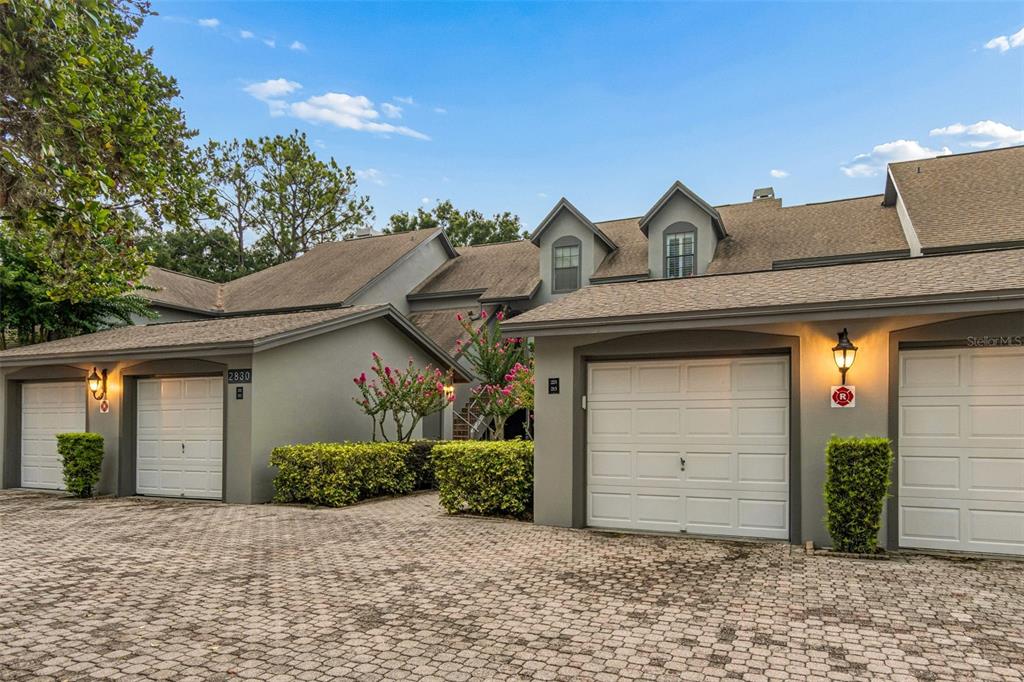 A multi-unit residential building features gray stucco walls, white garage doors, and a paved driveway — 2830 COUNTRYSIDE BOULEVARD UNIT 223, CLEARWATER, FL