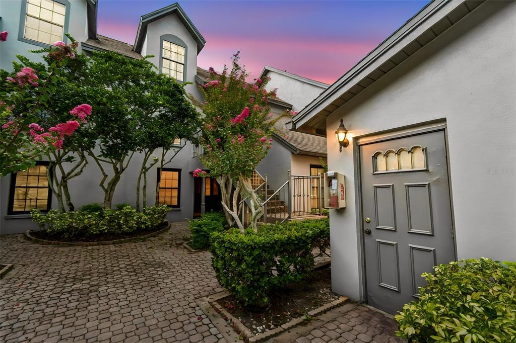 A paved courtyard features a gray door, lush landscaping, and multi-story buildings at dusk — 2830 COUNTRYSIDE BOULEVARD UNIT 223, CLEARWATER, FL