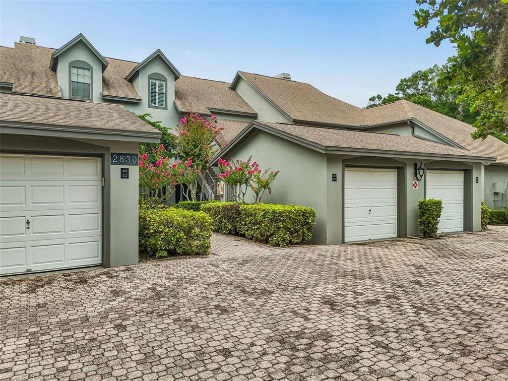 A multi-unit residential building features a paved driveway, three garage doors, and landscaped bushes — 2830 COUNTRYSIDE BOULEVARD UNIT 223, CLEARWATER, FL