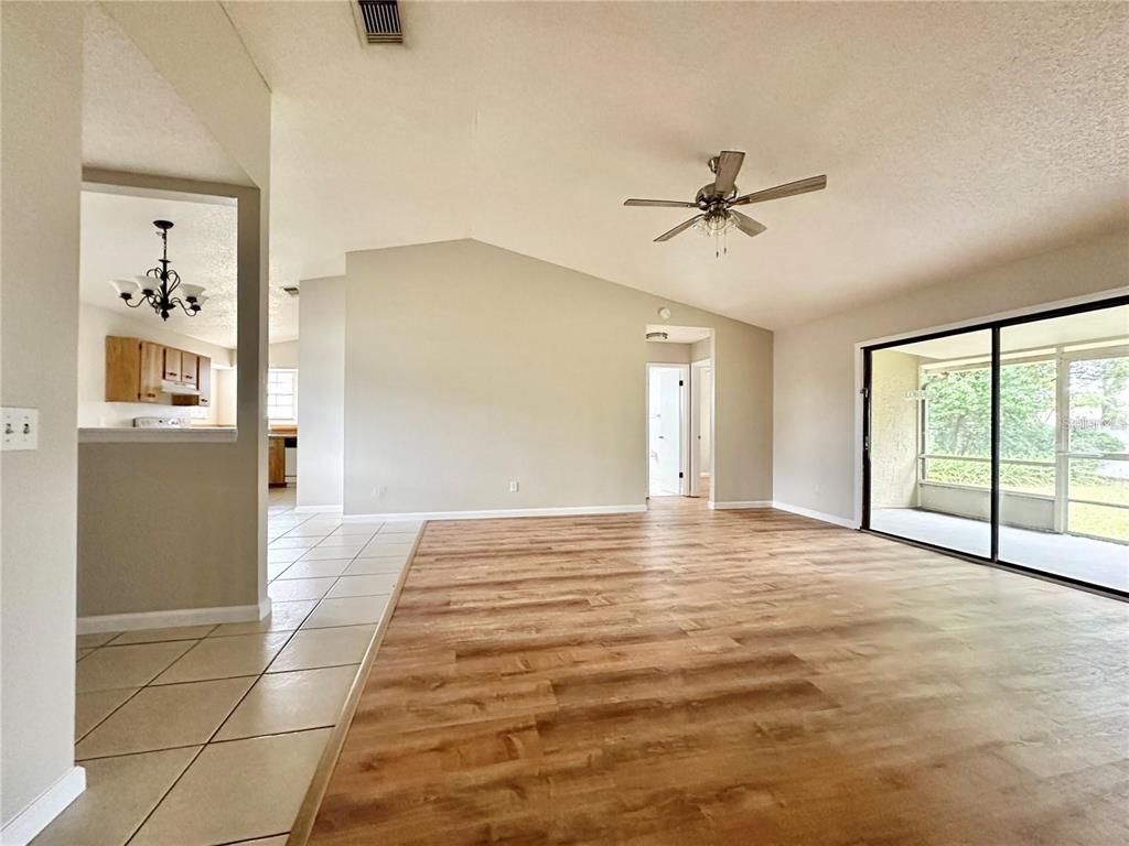 A living room with wood-look flooring, a vaulted ceiling, and a sliding glass door — 896 MENTMORE CIRCLE, DELTONA, FL