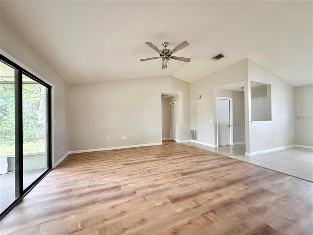 An empty living room features light wood-look flooring, a ceiling fan, and a sliding glass door — 896 MENTMORE CIRCLE, DELTONA, FL