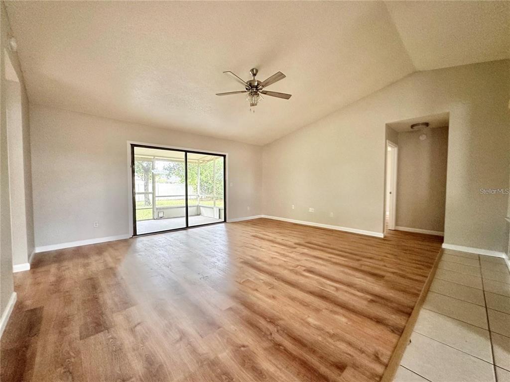 An empty living room features wood-look flooring, a vaulted ceiling with a fan, and sliding doors — 896 MENTMORE CIRCLE, DELTONA, FL