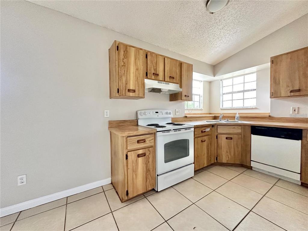 A kitchen features light wood cabinets, white appliances, and beige tile flooring — 896 MENTMORE CIRCLE, DELTONA, FL