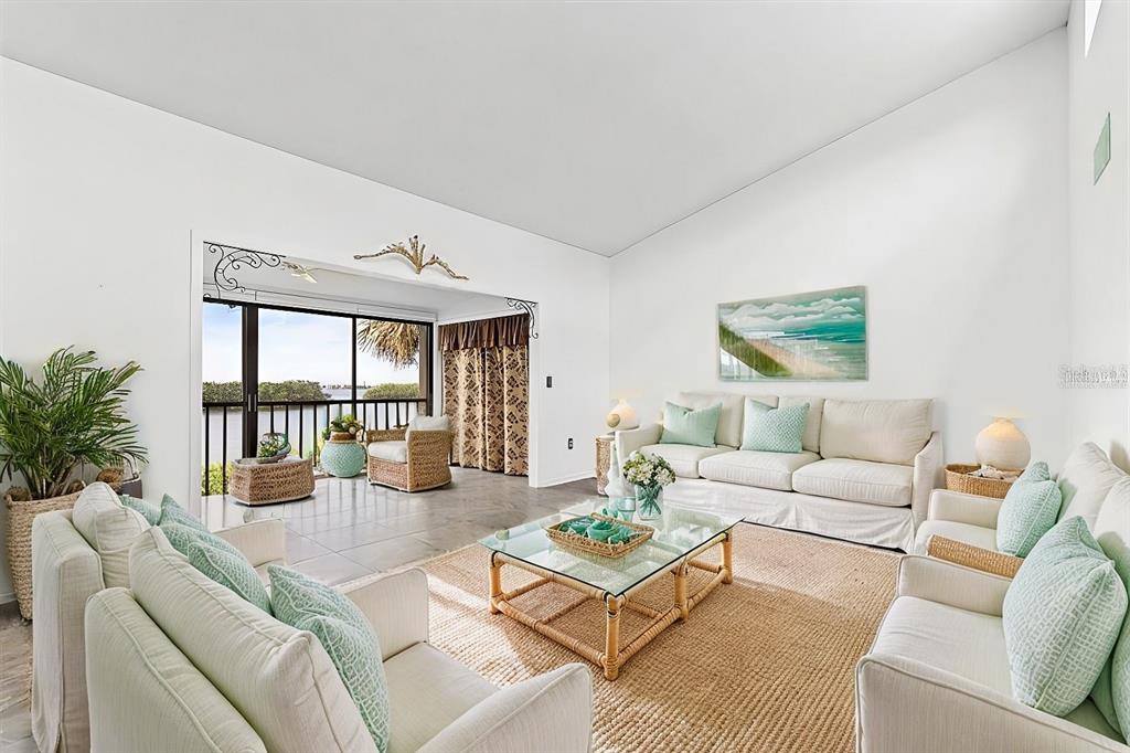 A bright living room features white sofas, a glass coffee table, and a balcony view — 1520 PELICAN POINT DRIVE UNIT BA251, SARASOTA, FL