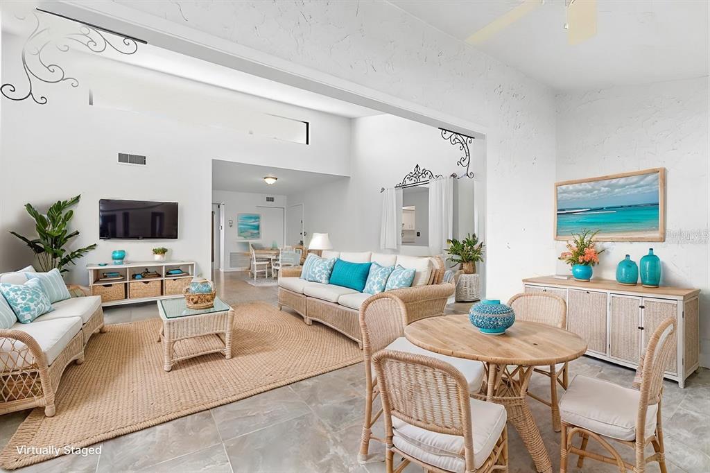 A bright living and dining area features wicker furniture, tile floors, and vaulted ceilings — 1520 PELICAN POINT DRIVE UNIT BA251, SARASOTA, FL