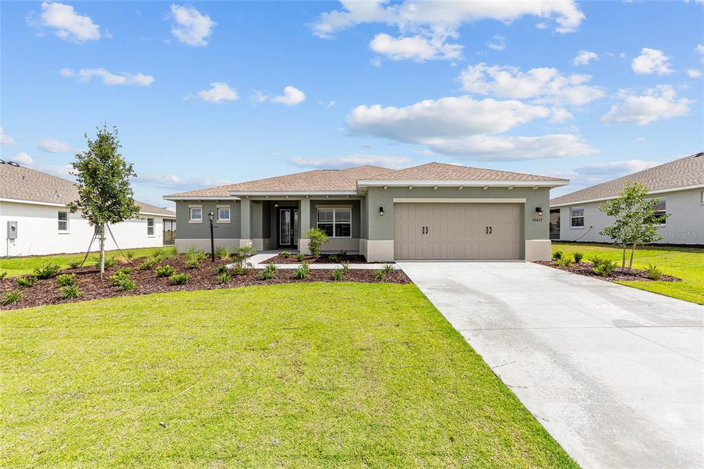 A single-story house with a tan garage, gray stucco exterior, and a concrete driveway — 10617 SW 101ST LANE ROAD, OCALA, FL