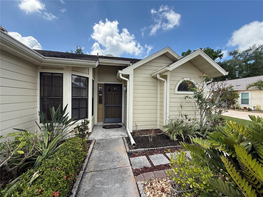 A beige house exterior features a concrete walkway leading to a dark brown front door — 5025 82ND WAY E, SARASOTA, FL